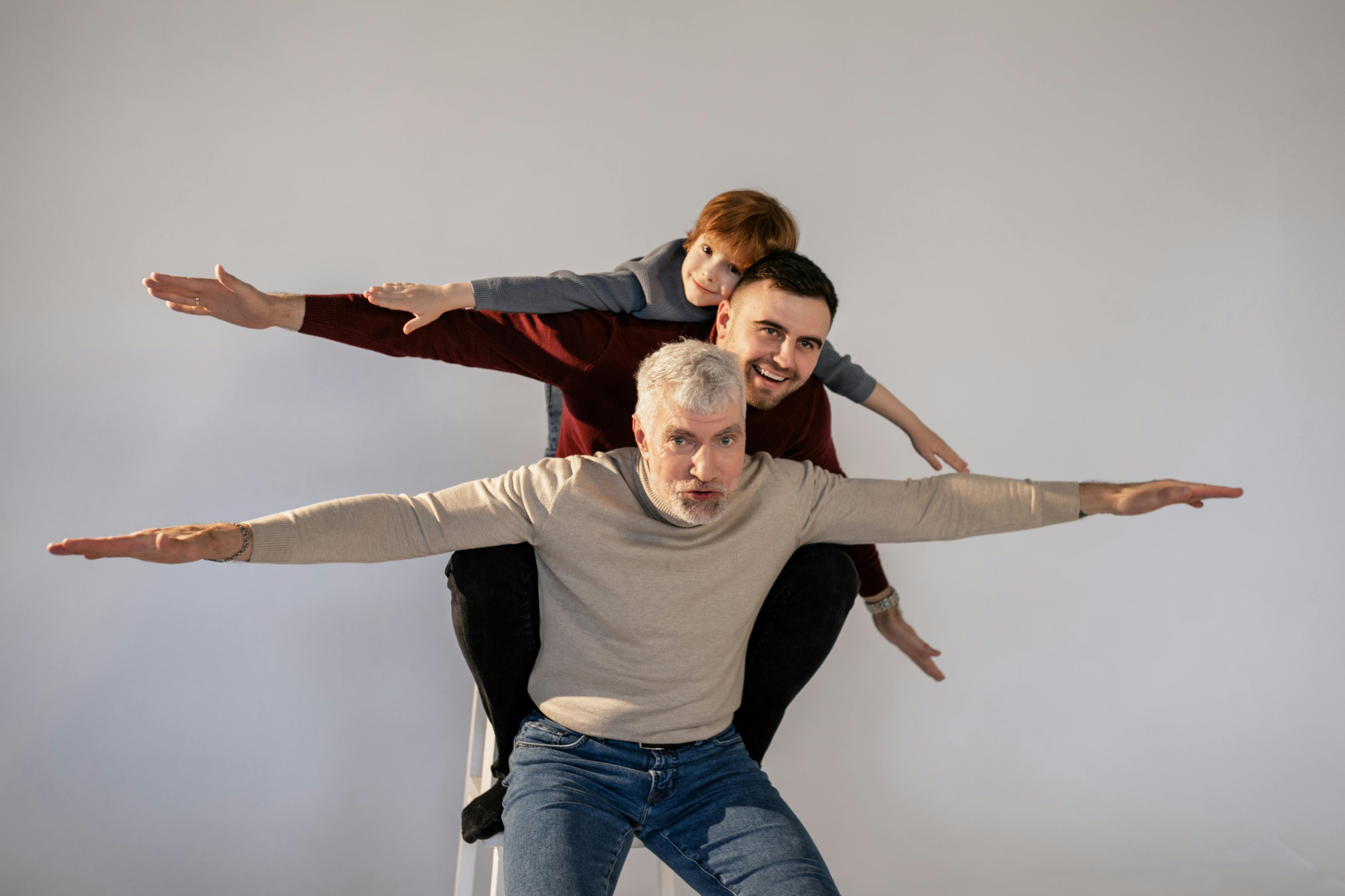 Three generations posing with outstretched arms in a playful studio shoot.